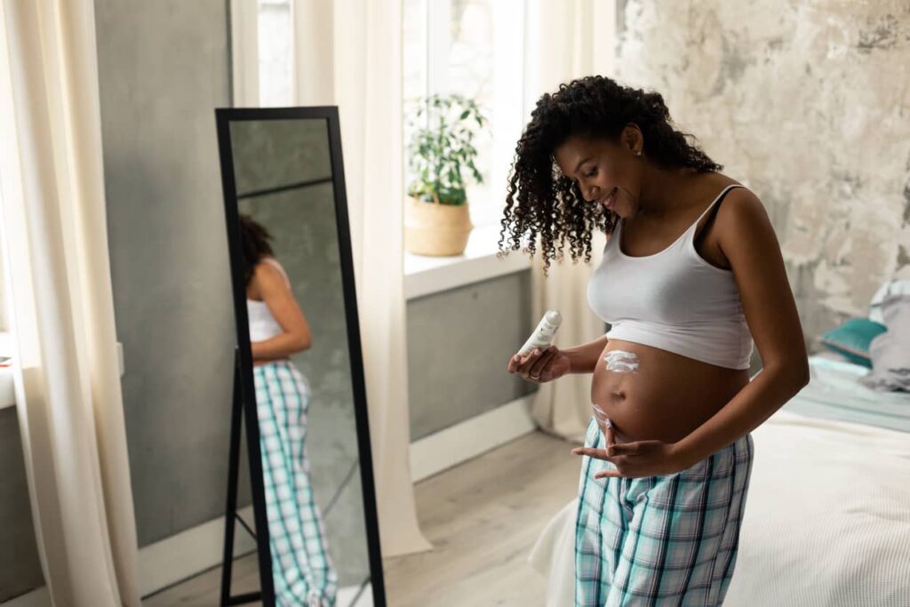 Mulher gestante passando creme na barriga